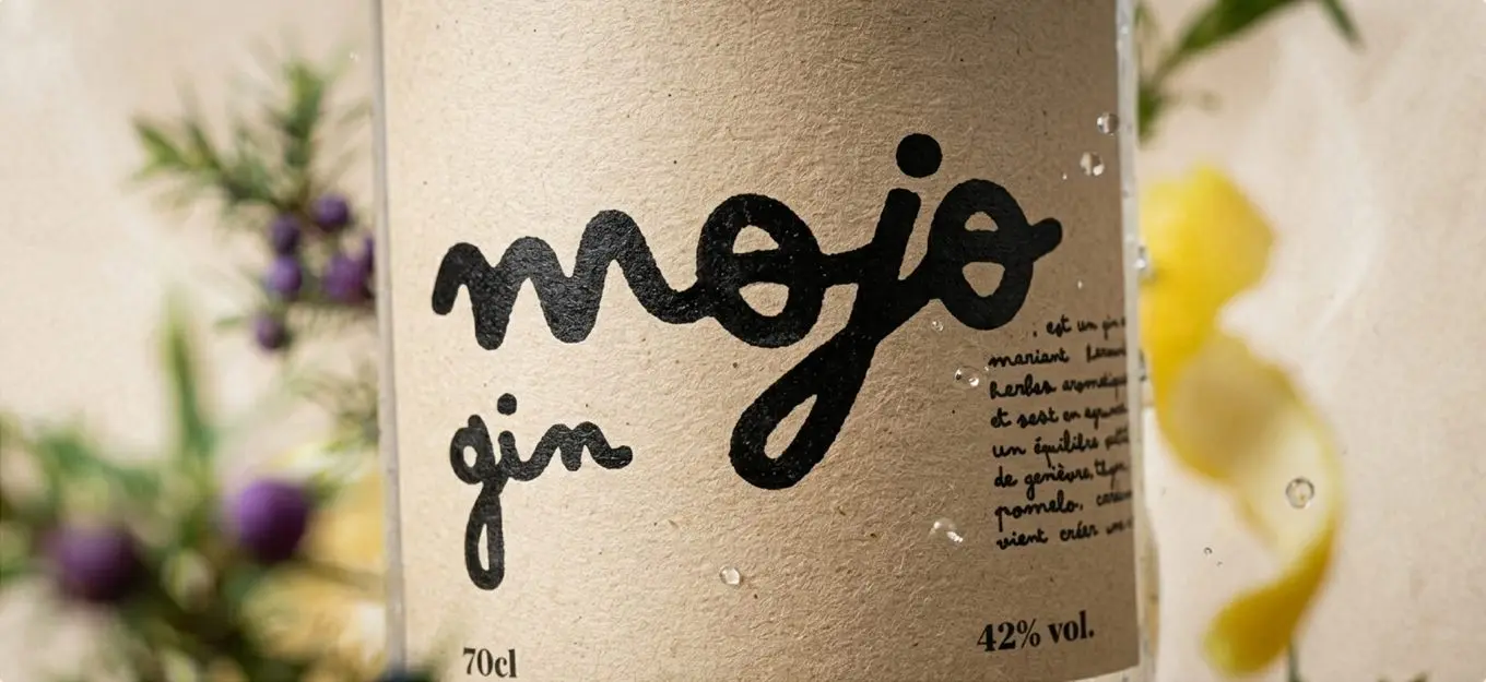 L'étiquette en papier kraft de la bouteille Mojo gin, lettrage noir tracé à la main, entre genièvre et zeste de citron.